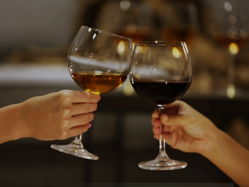 Hands hold a glass of red wine and a glass of white wine. The glasses are being clinked together.